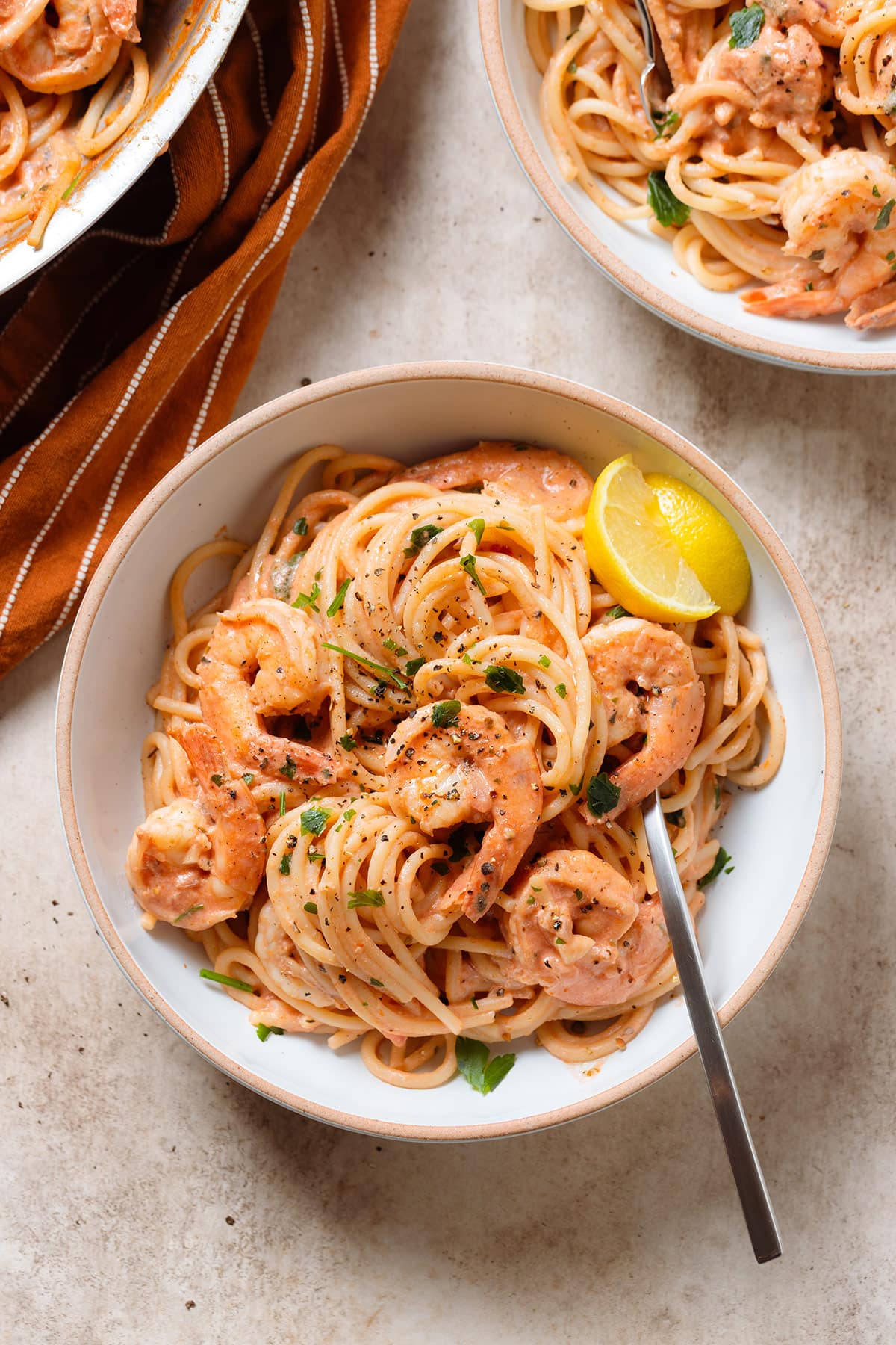 Creamy tomato pasta with shrimp in a low bowl garnished with fresh parsley and two wedges of lemon on the side of the bowl with a fork inserted in.