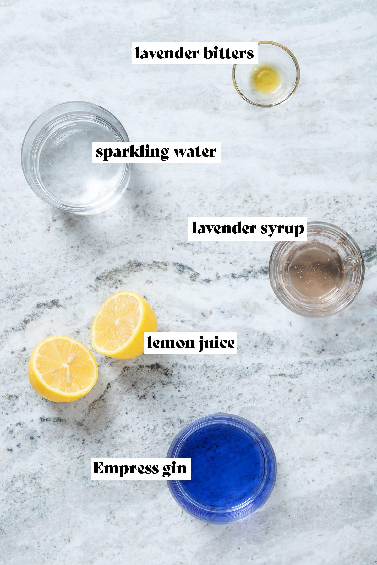 Lemon, gin, syrup, and bitters all measured out and laid out on a grey background with text overlay.