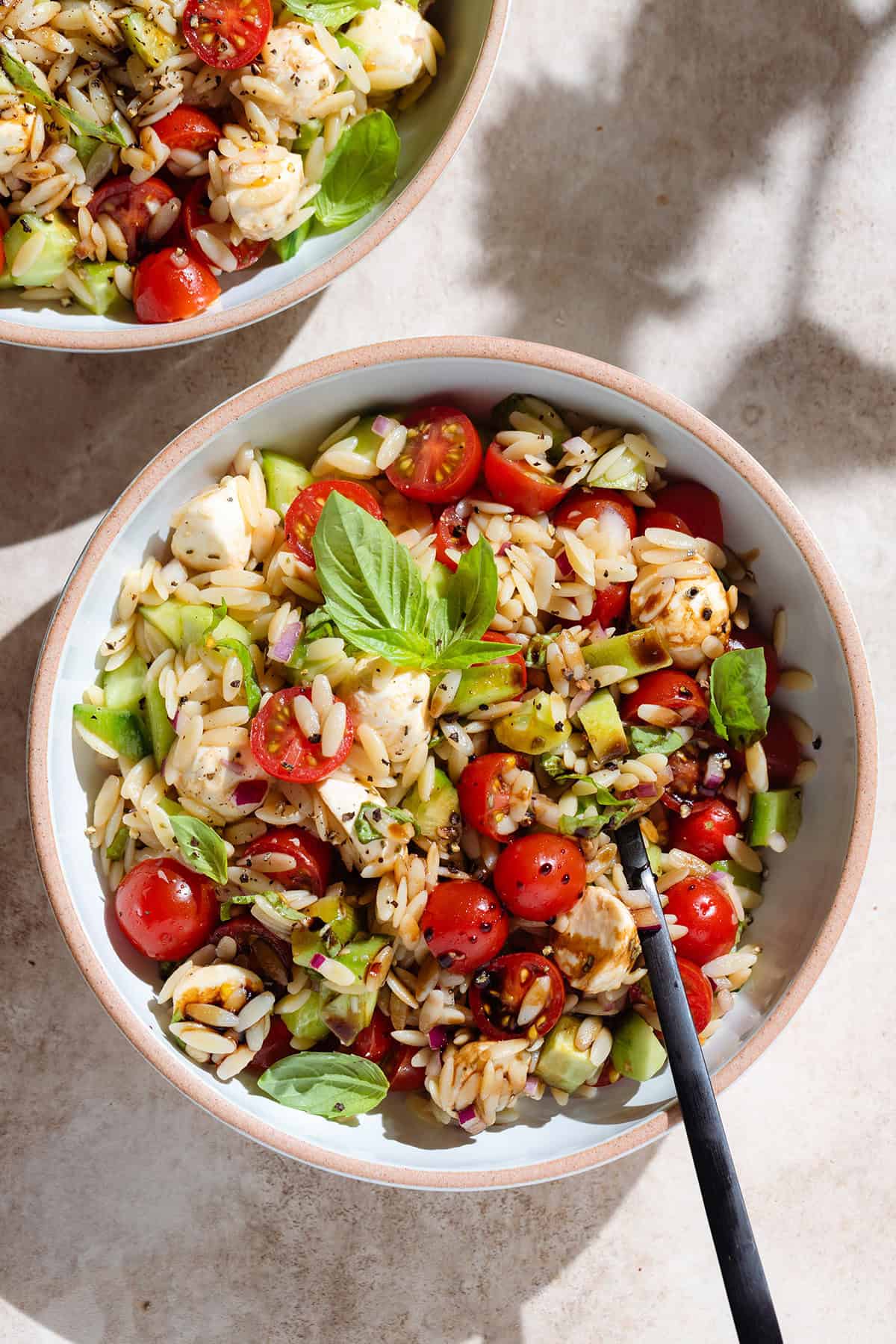 Orzo Caprese Salad with mini mozzarella balls in a low bowl garnished with fresh basil, balsamic glaze, and black pepper.