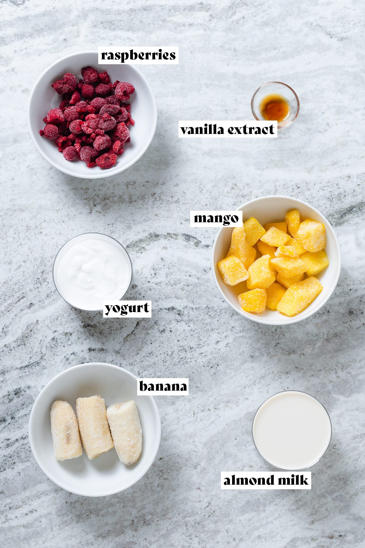 Frozen raspberries, mango, banana, yogurt, and other ingredients all measured and laid out in small bowls with text overlay.