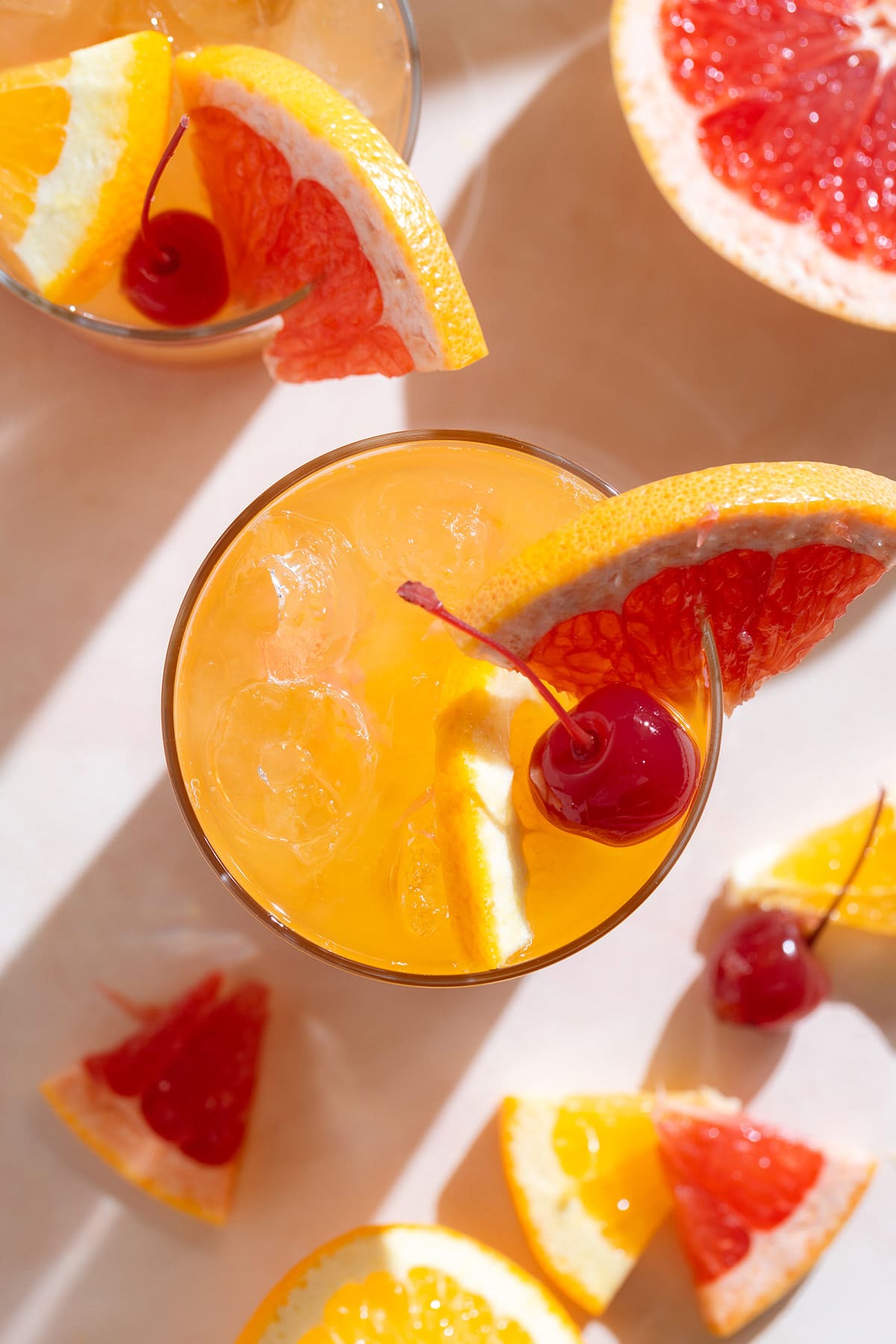 A tequila sunset cocktail in a tall glass with orange juice garnished with a cocktail cherry and a slice of grapefruit.