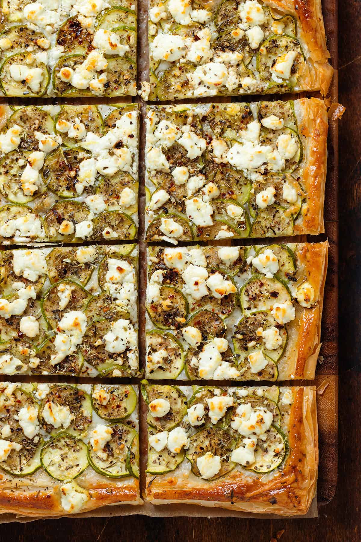 Baked zucchini puff pastry tart sliced into squares on a wooden cutting board.