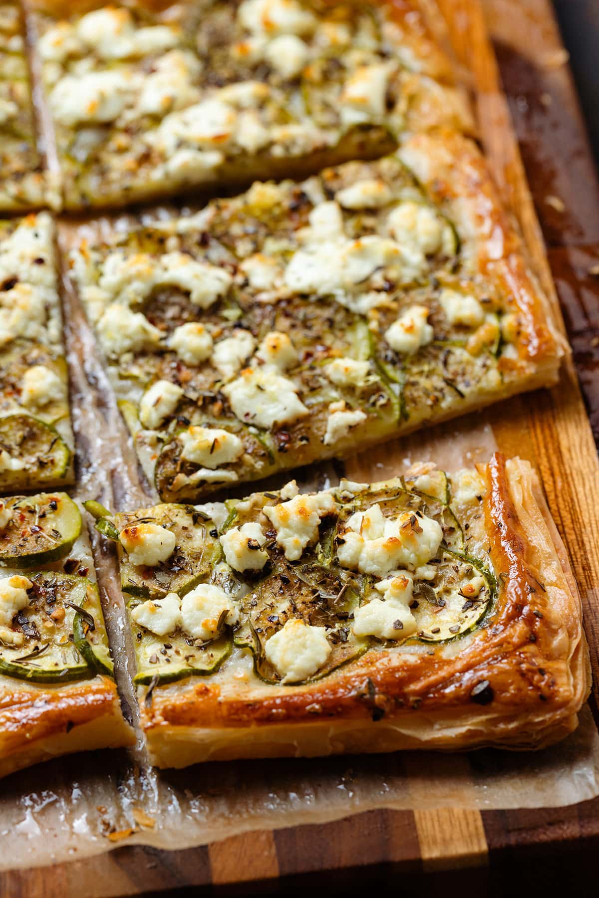 Crispy baked zucchini puff pastry tart sliced into squares on a wooden cutting board.