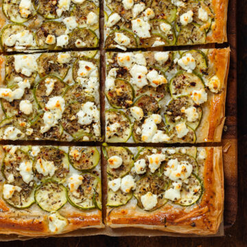 Baked zucchini puff pastry tart sliced into squares on a wooden cutting board.