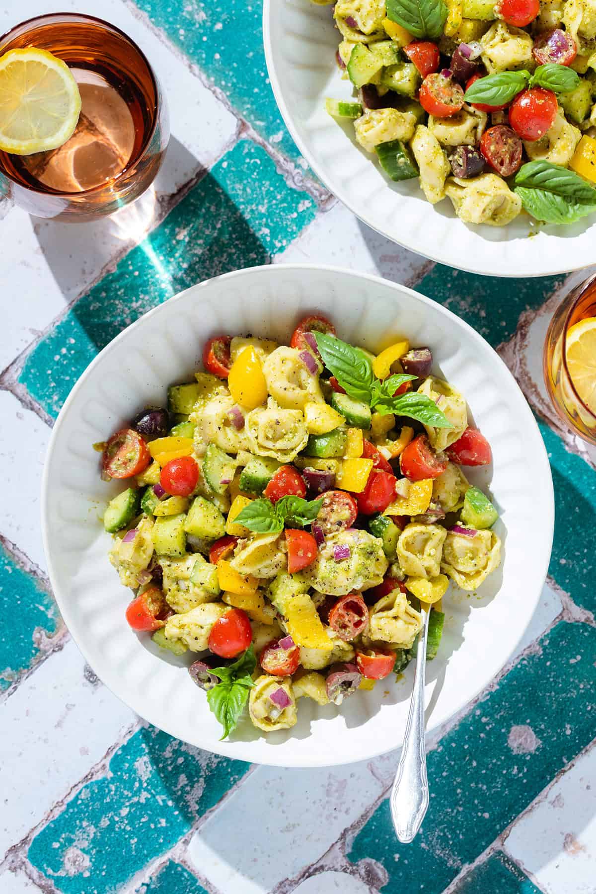 Tortellini pesto salad with fresh chopped veggies and basil in a white bowl with a silver fork in the bowl.