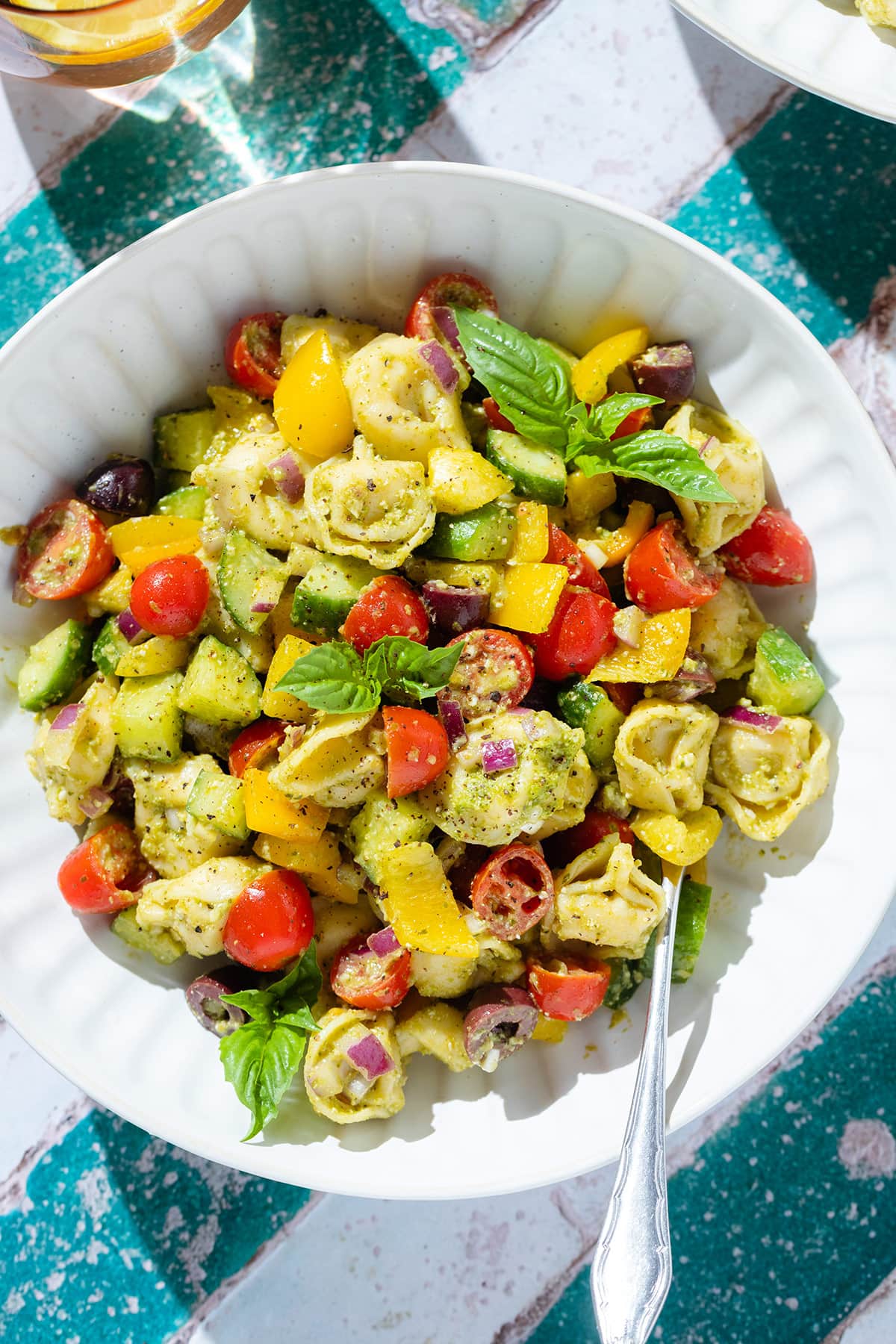 Tortellini pesto salad with fresh chopped veggies and basil in a white bowl with a silver fork in the bowl.