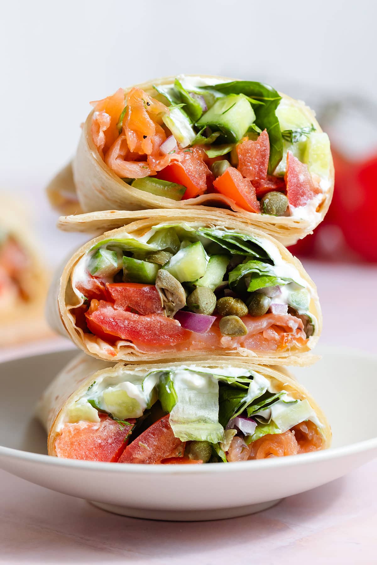Three smoked salmon veggie wraps cut in half showing the inside stacked on top of each other on a small plate.
