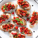 Strawberry bruschetta with cream cheese and fresh basil on a white serving plater with a black rim.