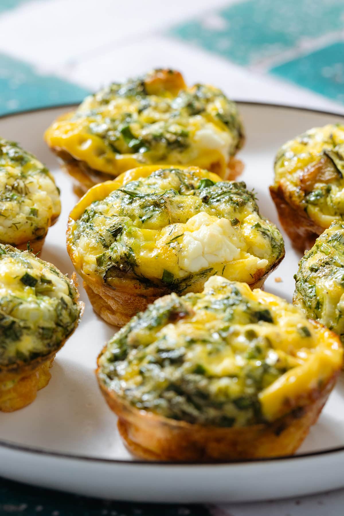 Zucchini egg muffins with feta and herbs on a white plate with a black rim.