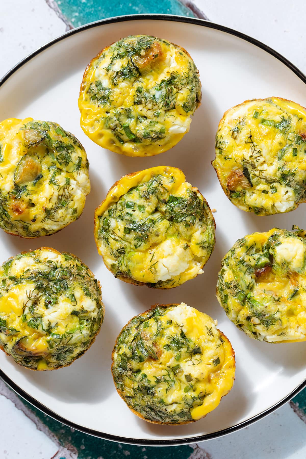 Zucchini egg muffins with feta and herbs on a white plate with a black rim.