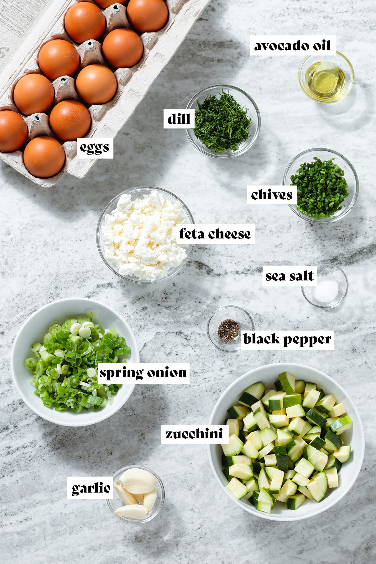 Ingredients like eggs, zucchini, spring onion, and herbs all measured and laid out in small glass bowls with text overlay.