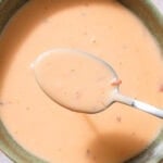 Orange creamy sauce in a green bowl with a spoon with the sauce showing it held over it.