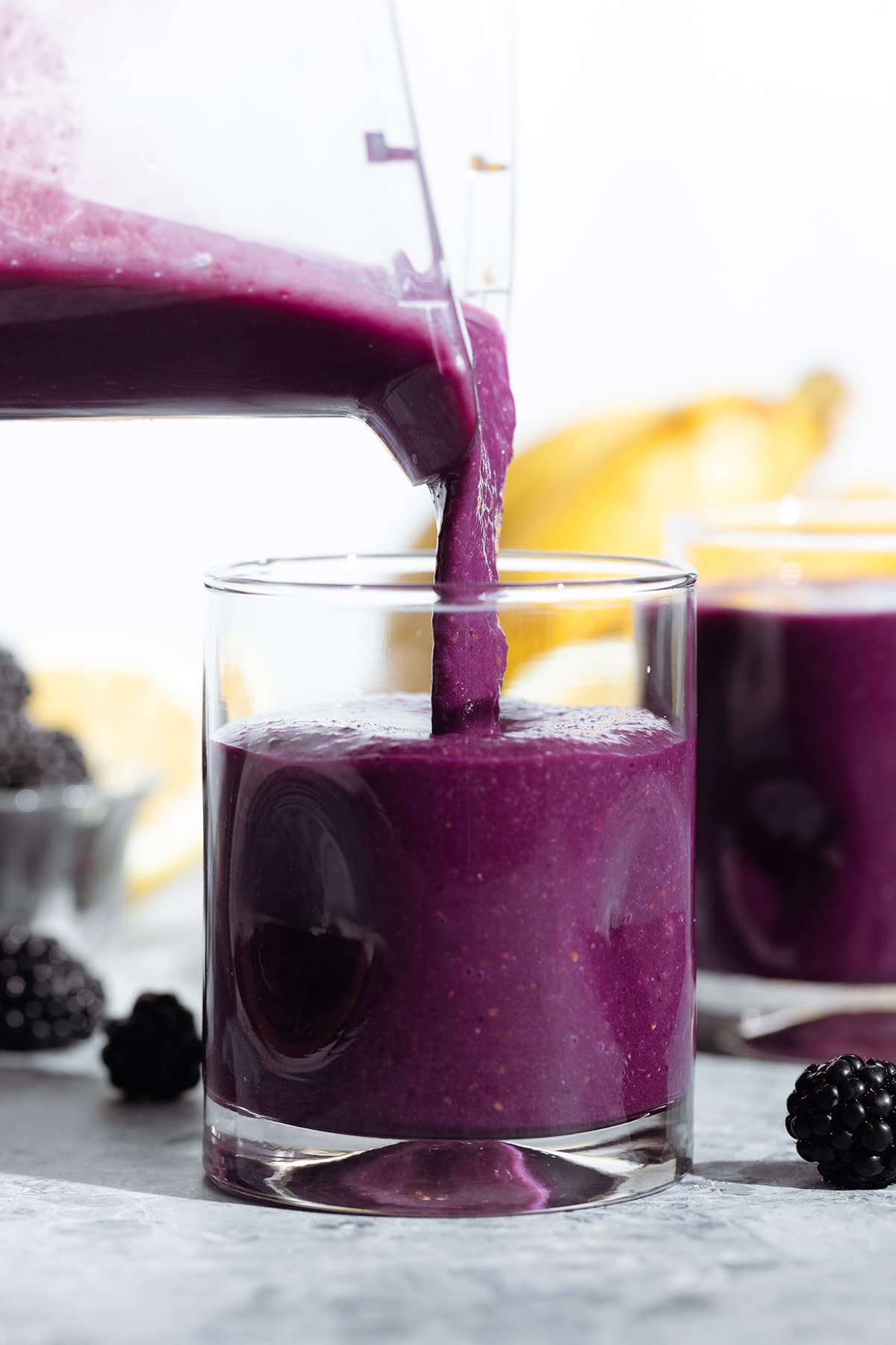 Bright purple smoothie being poured into a short glass from a high speed blender.