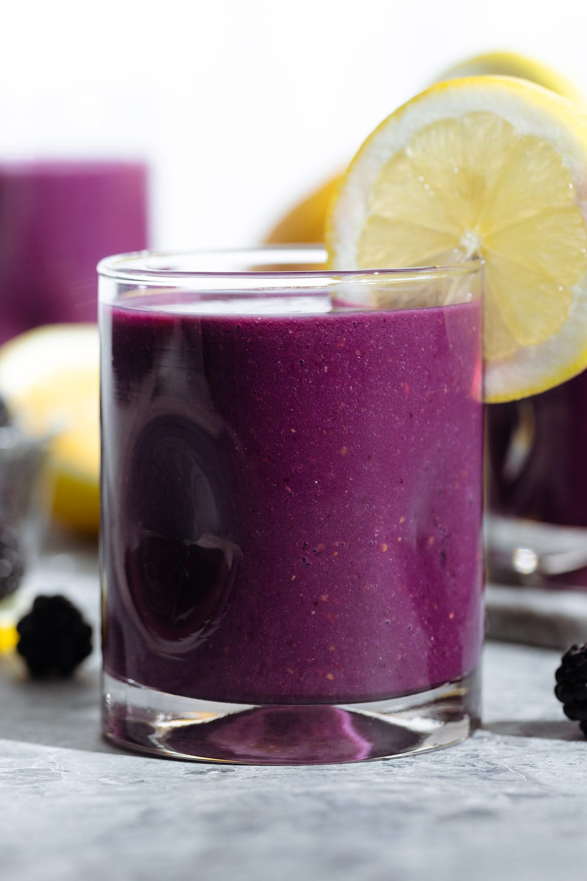 Dark purple smoothie in a short glass garnished with a slice of lemon.