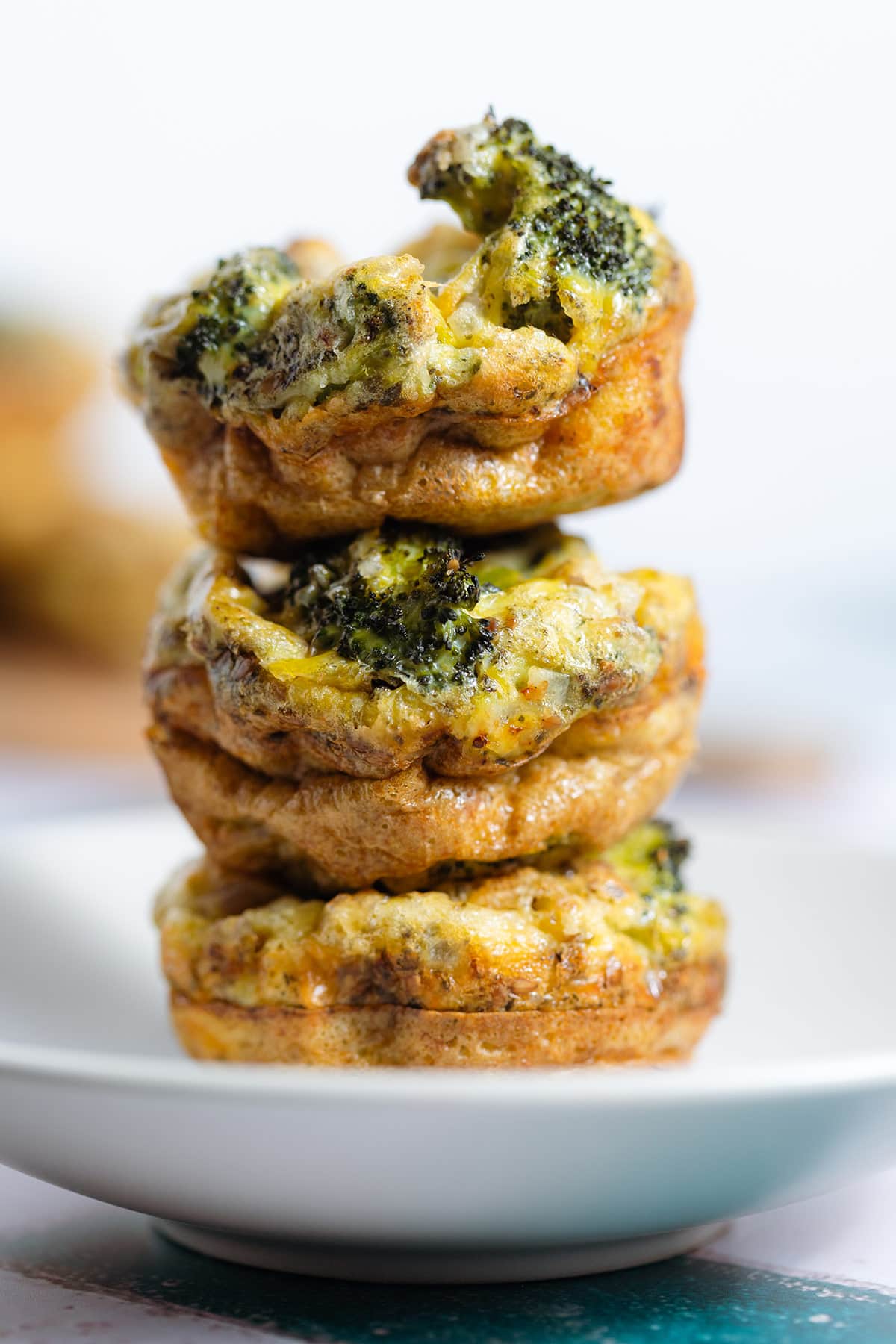 Three golden cheesy egg muffins with broccoli and cheddar stacked on top of each other.