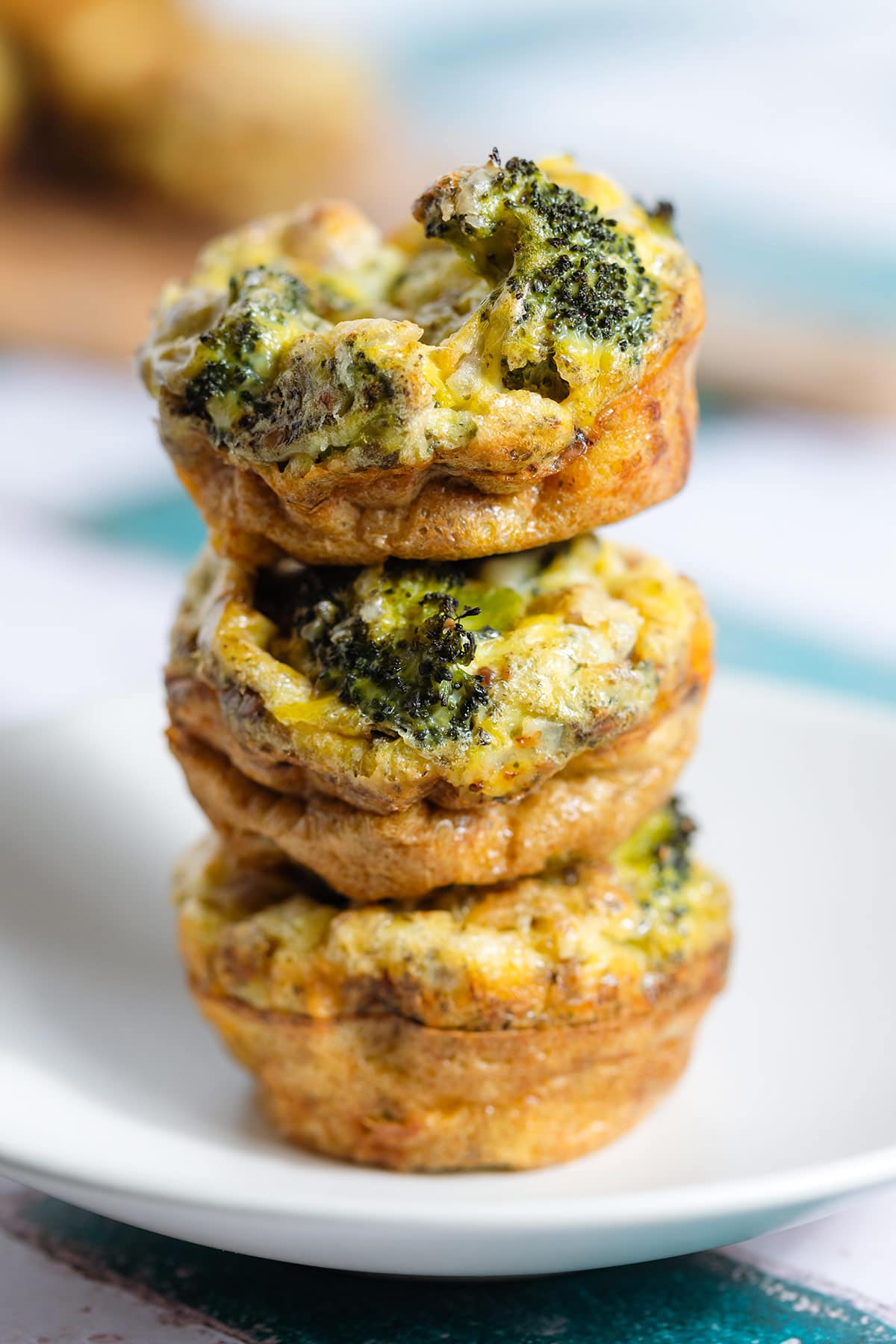 Three golden cheesy egg muffins with broccoli and cheddar stacked on top of each other.