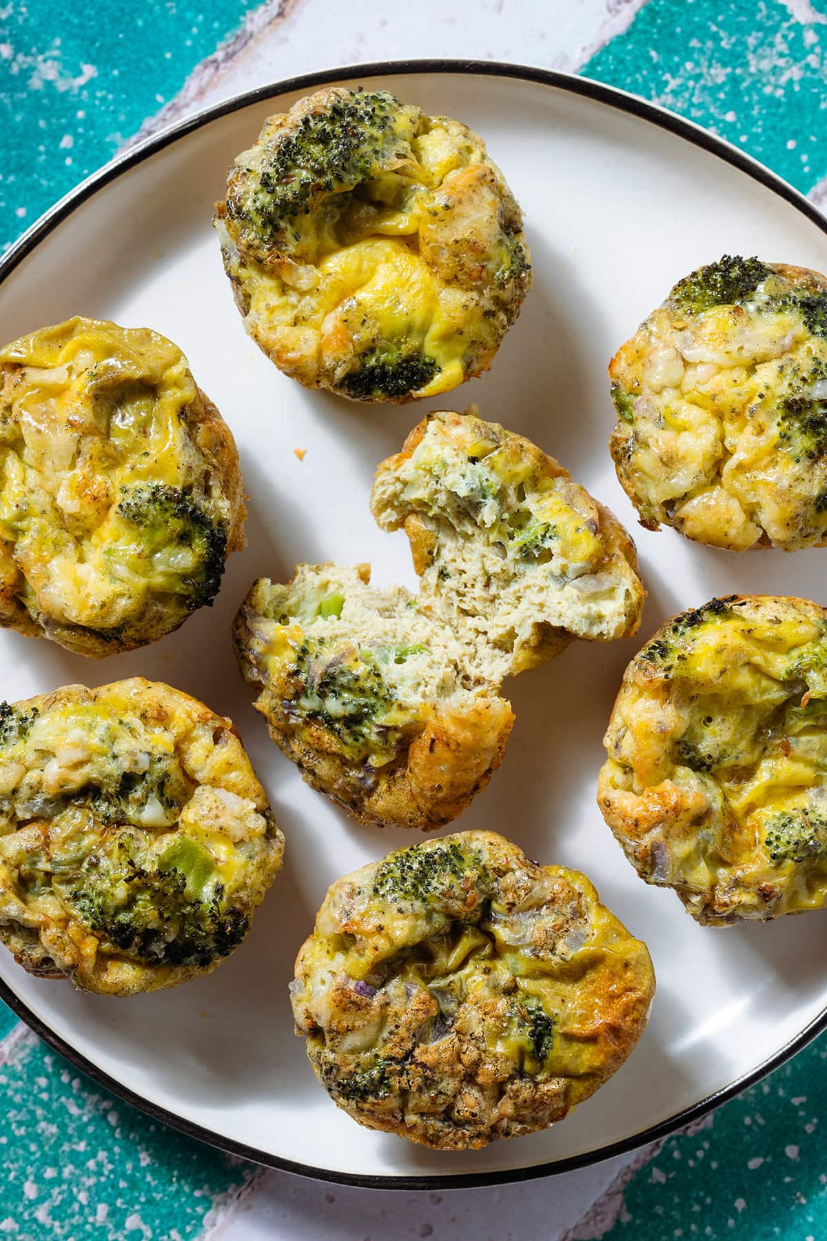 Broccoli egg muffins on a large white plate with the middle one sliced in half to show the inside.