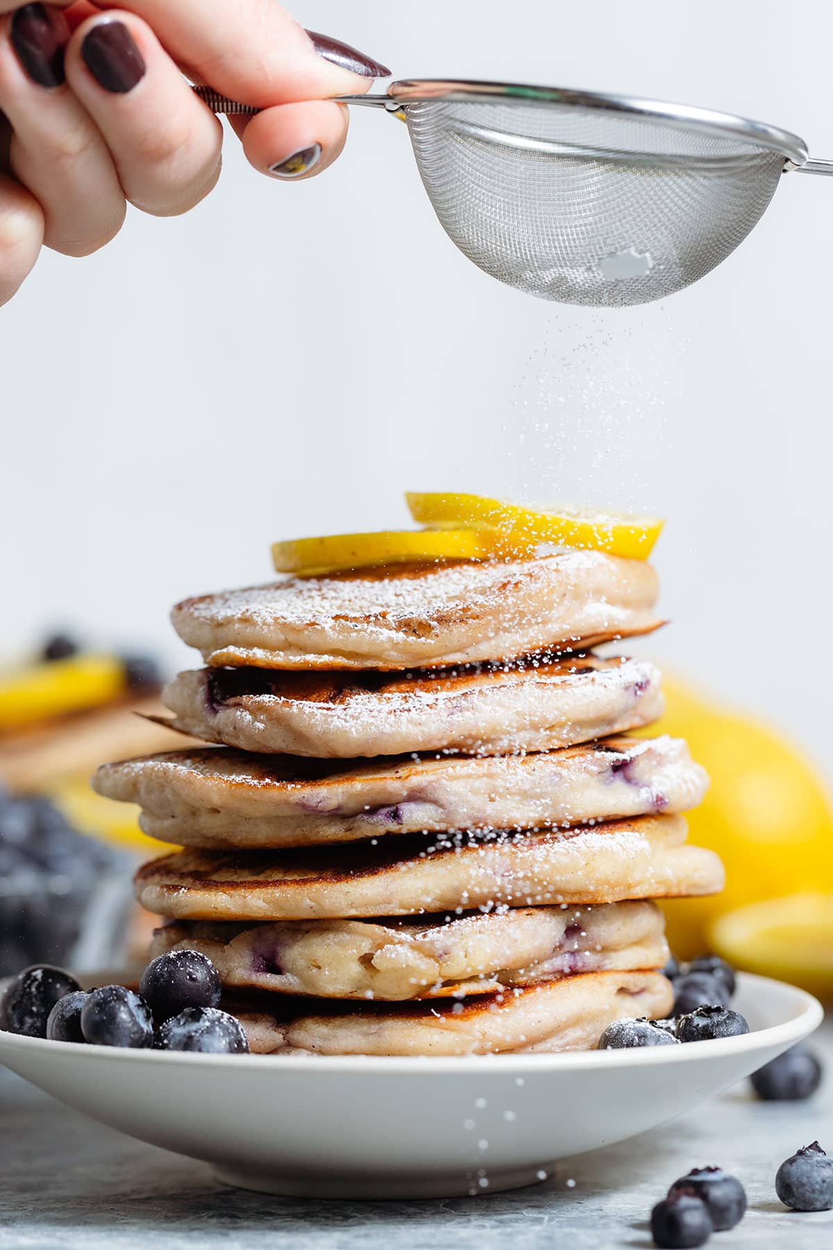 A stack of blueberry pancakes being dusted with powdered sugar.
