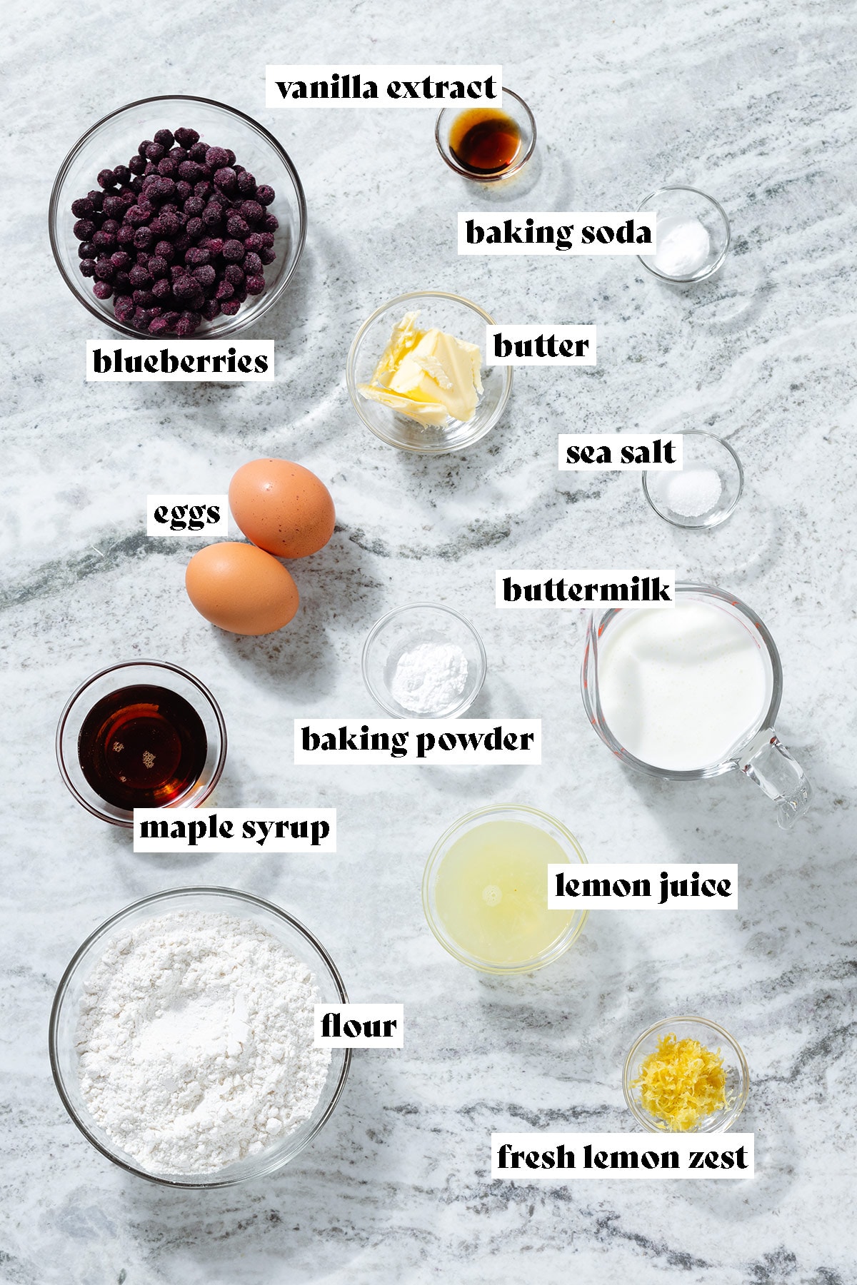 Measured ingredients in small glass bowls like blueberries, flour, butter, milk, and lemon juice with text overlay.