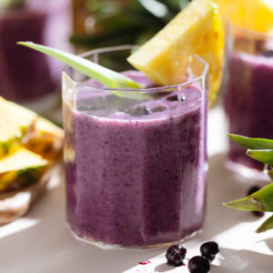 Purple smoothie in a short glass garnished with fresh pineapple and a pineapple leaf.