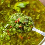 A spoon holding chopped fresh cilantro sauce with oil and fresh chili.