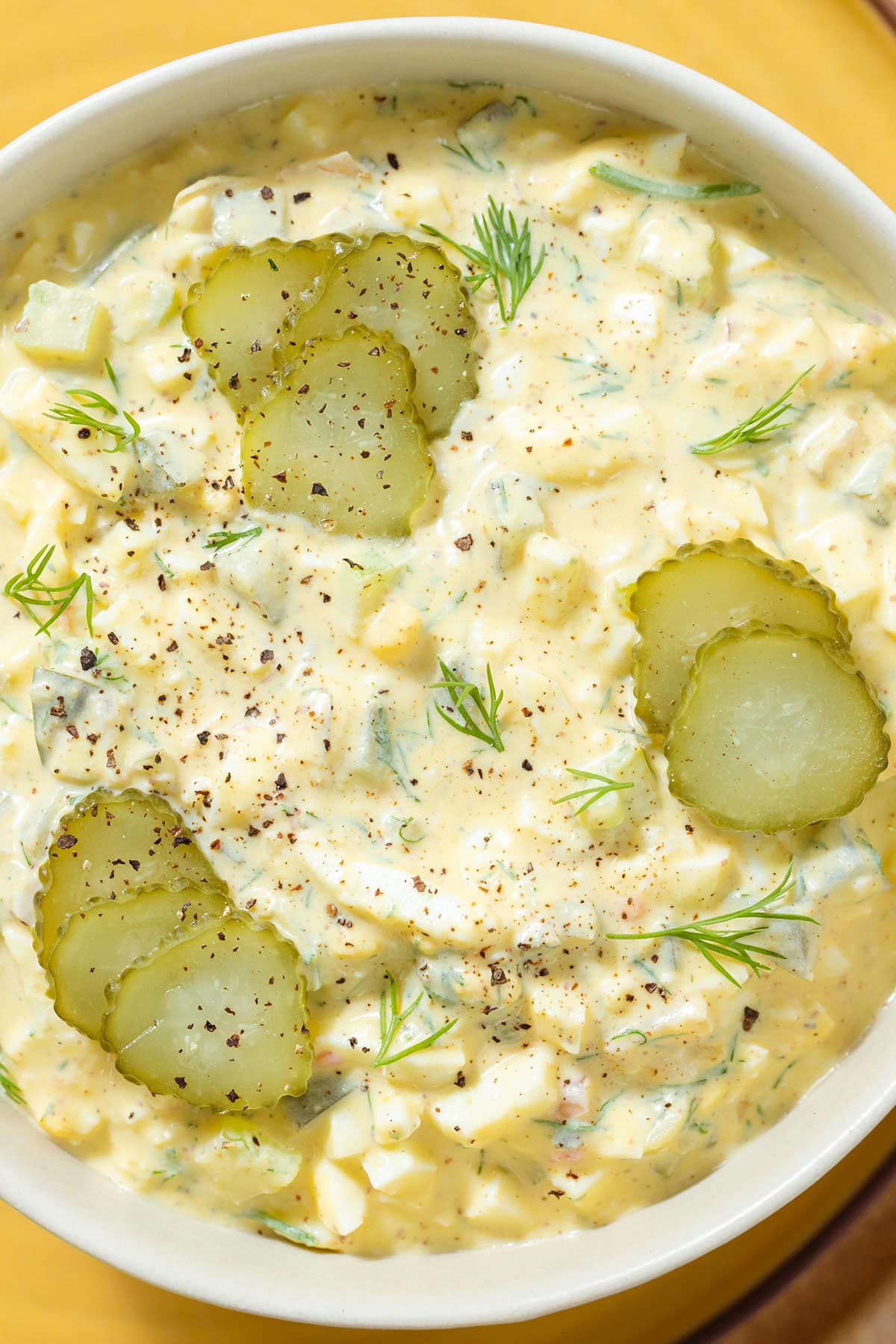 Egg salad in a white bowl garnished with pickles and dill.