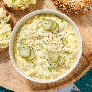 Egg salad in a white bowl garnished with pickles and dill.