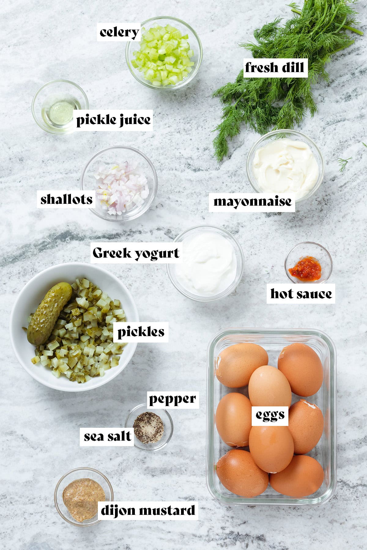 Ingredients like eggs, pickles, fresh dill, and shallots laid out and measured in small glass bowls.