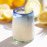 A light yellow smoothie in a short glass with a blue rim garnished a lemon slice.