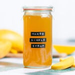 Bright yellow syrup in a tall glass jar with a black label that says mango simple syrup.