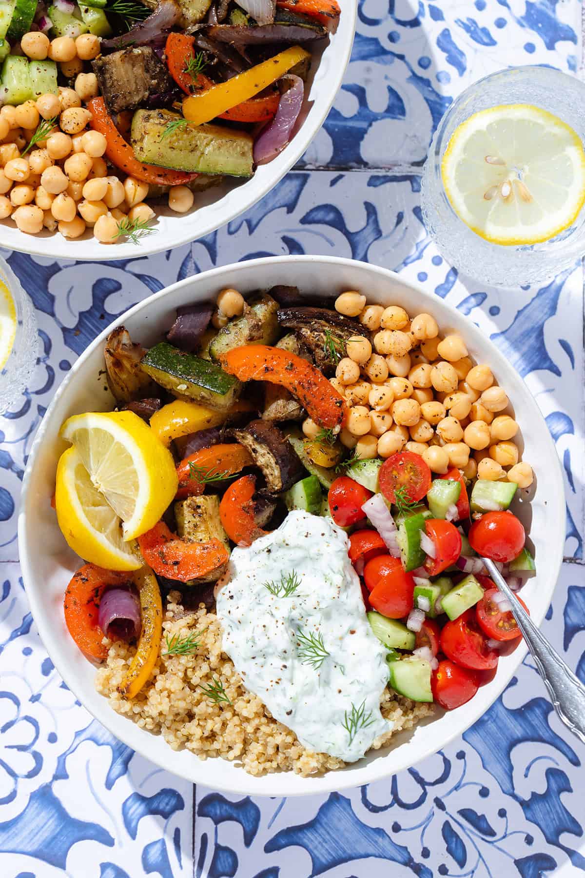 Quinoa bowl with roasted vegetables, chickpeas, fresh salad, and tzatziki in white bowls.