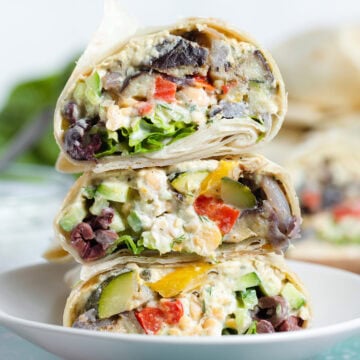 A stack of 3 veggie wraps sliced in the middle on a small white plate.