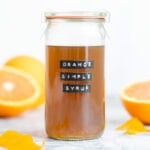 Orange syrup in a tall glass jar with a black label that says orange simple syrup.