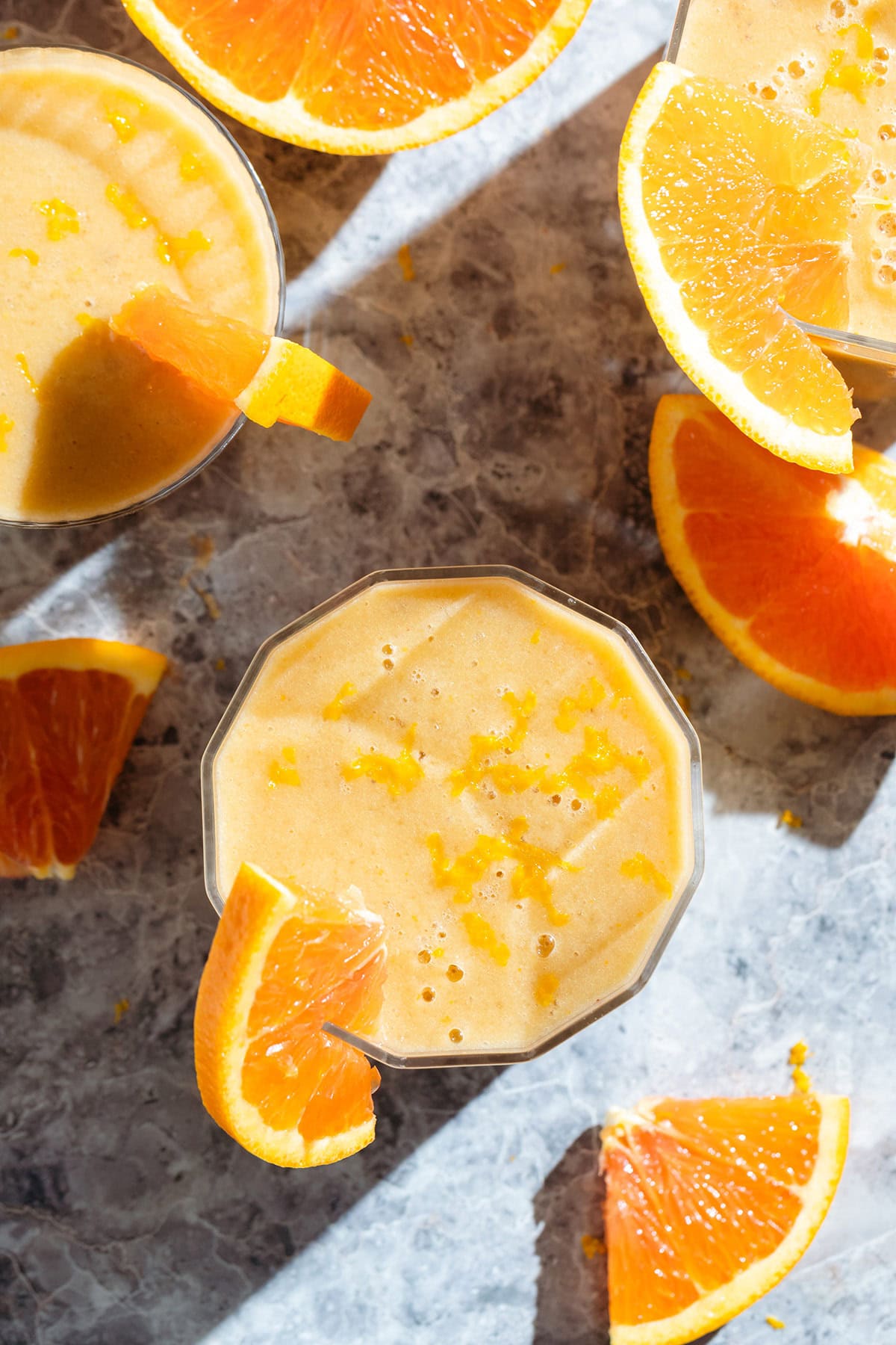 Bright orange smoothie in small glasses garnished with slices of fresh orange and orange zest.