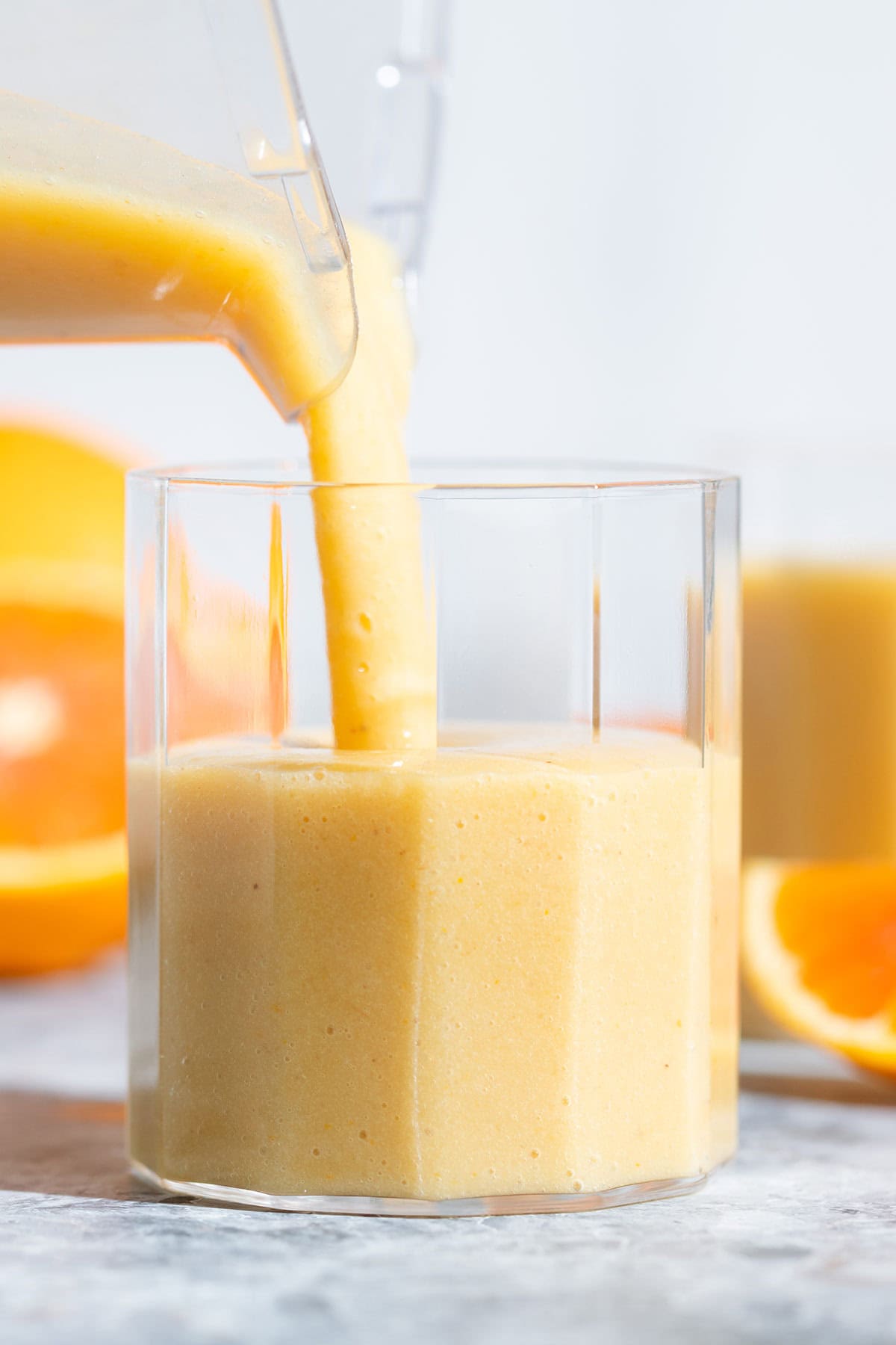 Orange smoothie being poured into a small glass.