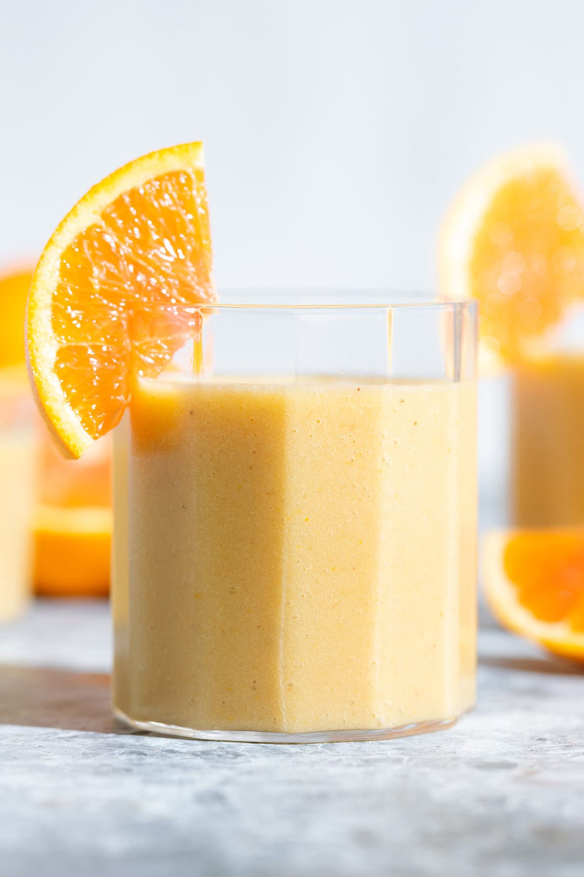 Bright orange smoothie in a small glass garnished with a slice of fresh orange.