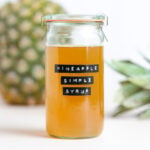 Yellow syrup in a tall glass jar with a label that says pineapple simple syrup.