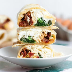 Egg white wraps with spinach and sundried tomatoes stacked on a small plate.