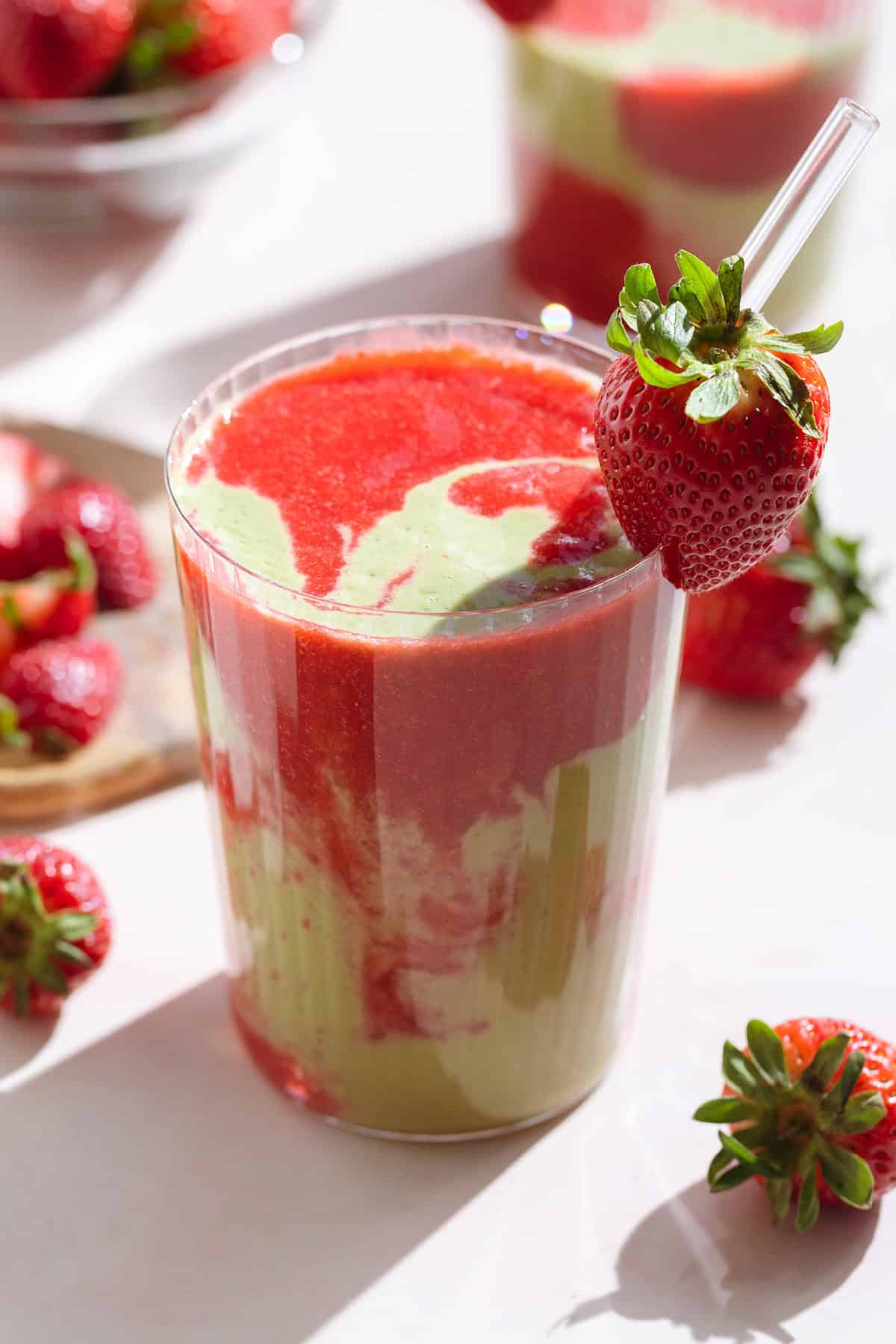 Red and green smoothie in a tall glass garnished with a fresh strawberry and a glass straw.