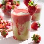 Bright red and green smoothie in a tall glass garnished with a fresh strawberry.