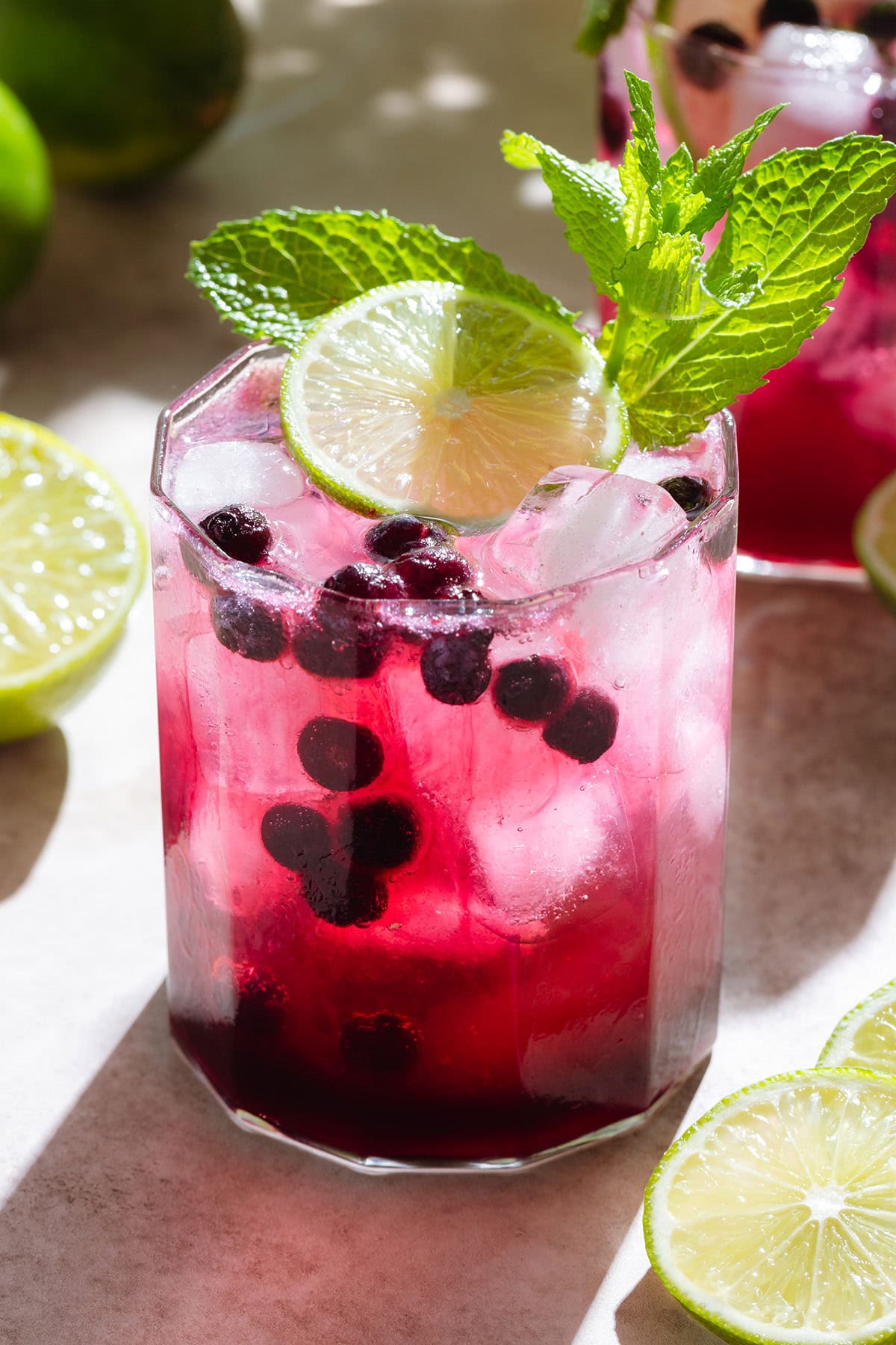 Bright purple blueberry mocktail in a short glass with ice and sparkling water on top creating a layered effect garnished with fresh lime and mint.