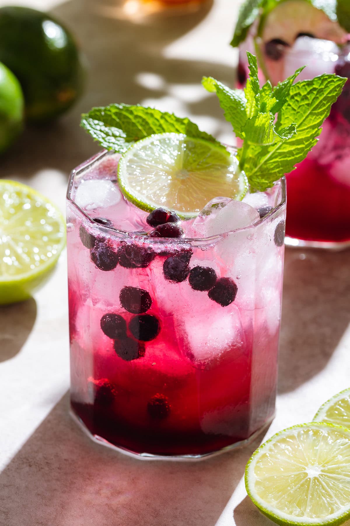 Bright purple blueberry mocktail in a short glass with ice and sparkling water on top creating a layered effect garnished with fresh lime and mint.