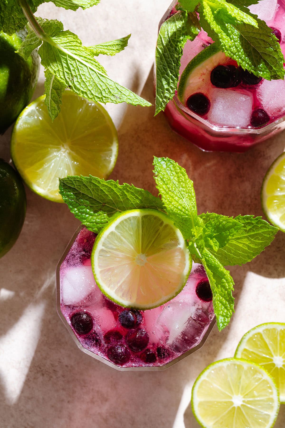 Bright purple blueberry mocktail in a short glass with ice garnished with fresh lime and mint.