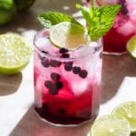 Bright purple blueberry mocktail in a short glass with ice and sparkling water on top creating a layered effect garnished with fresh lime and mint.