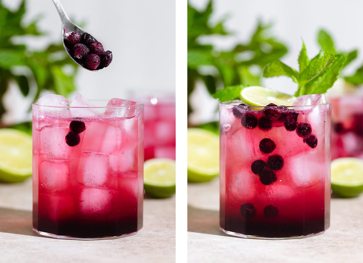 Frozen wild blueberries being added to a short glass with bright purple mocktail garnished with fresh mint and lime.