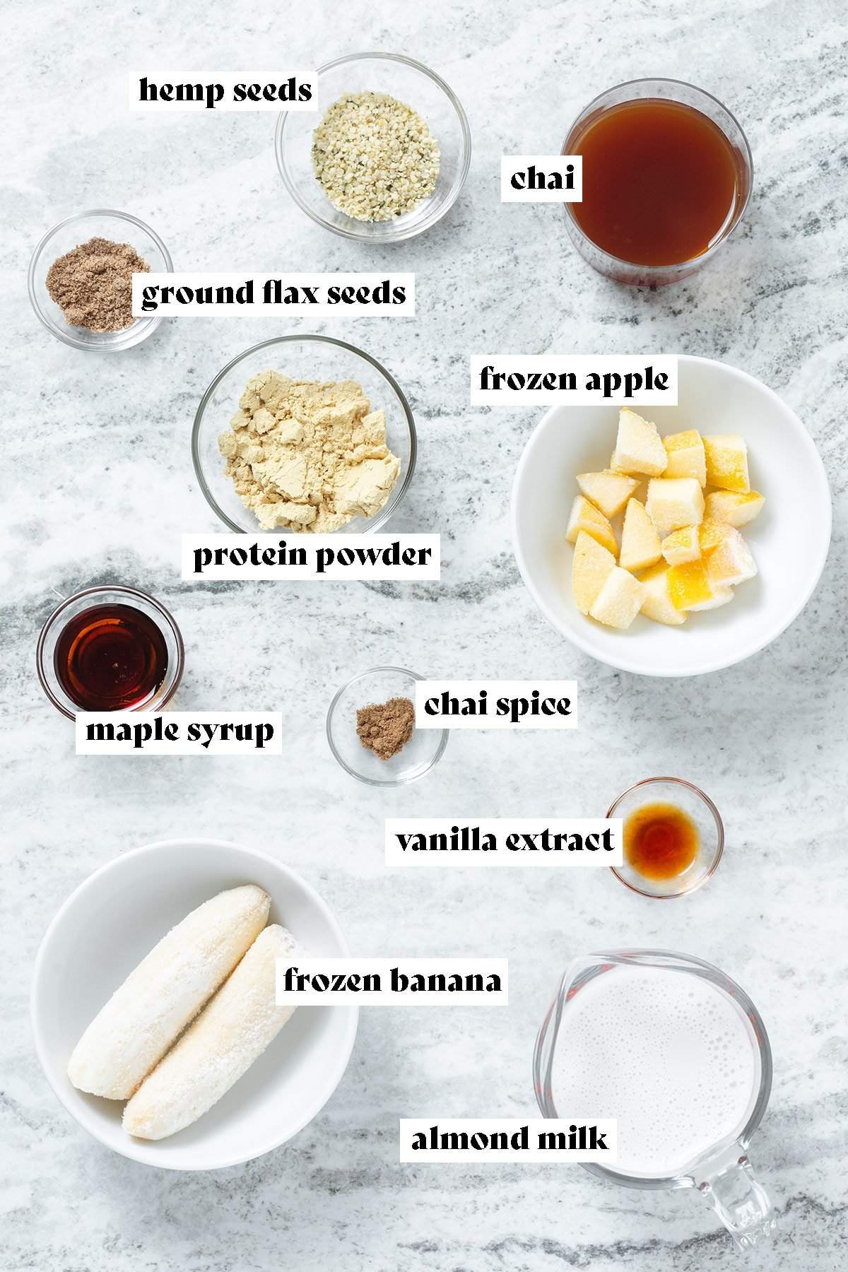 Smoothie ingredients like frozen banana, milk, frozen apple, chai, and protein powder laid out in small bowls.