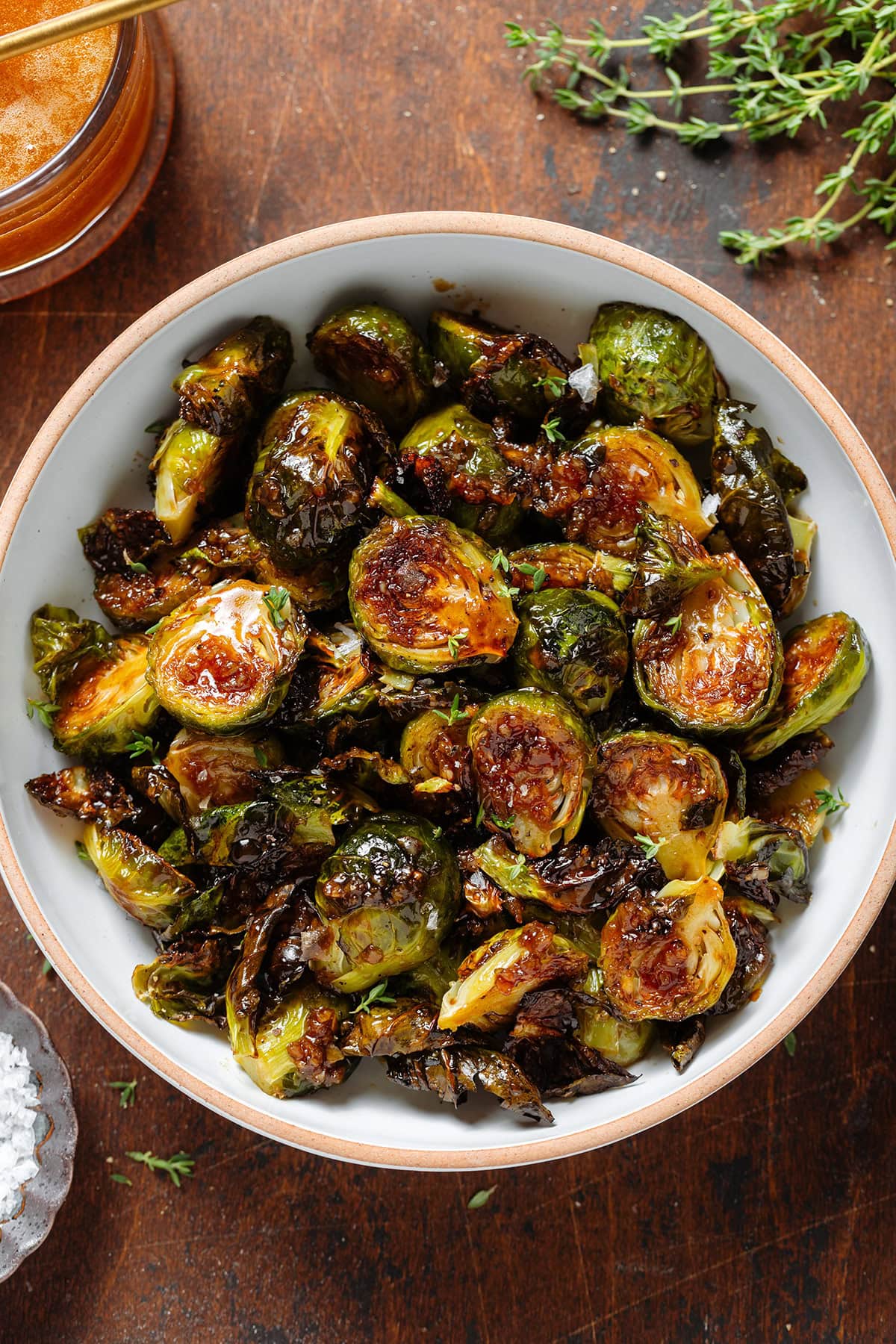 Crispy saucy golden brussels sprouts in a white bowl with a brown rim sprinkled with salt flakes and fresh thyme.