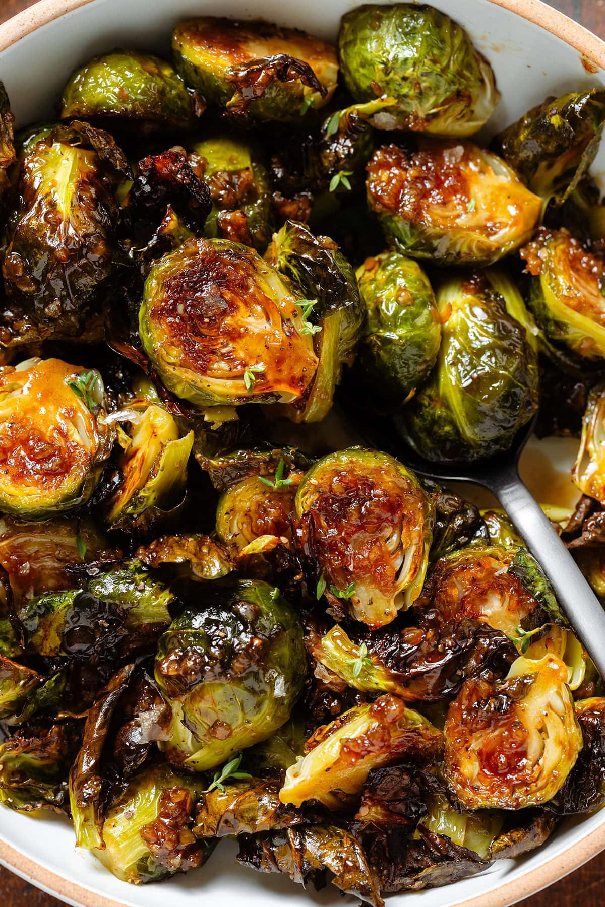 Crispy saucy golden brussels sprouts with sprinkled with salt flakes and fresh thyme and a spoon inserted on the right.