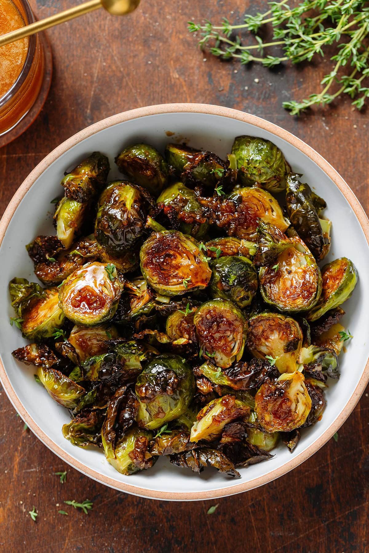 Crispy saucy golden brussels sprouts in a white bowl with a brown rim sprinkled with salt flakes and fresh thyme.