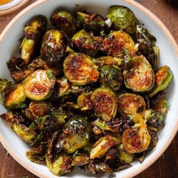 Crispy saucy golden brussels sprouts in a white bowl with a brown rim sprinkled with salt flakes and fresh thyme.